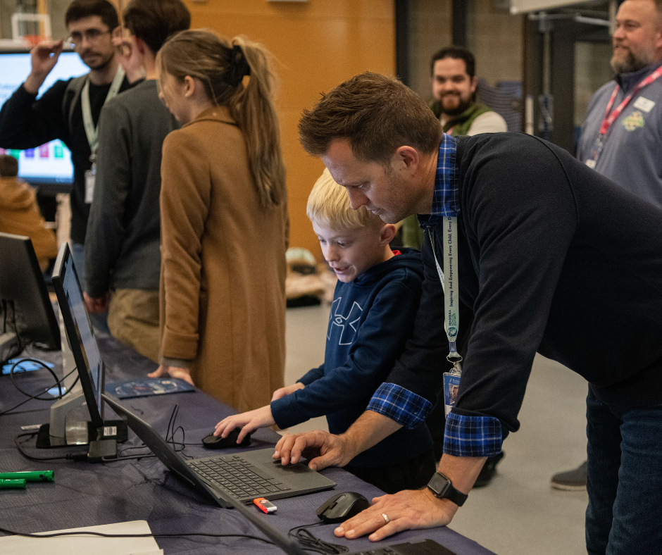 teacher hovered over laptop with student working and other educators looking on